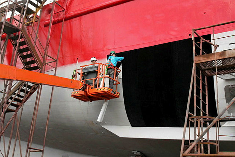 Two workers applying sheet of Finsulate to large ship